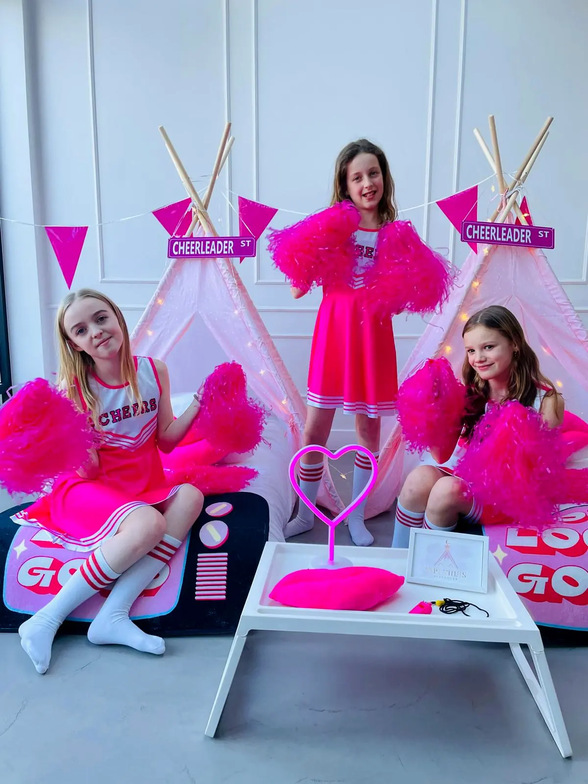 Drie cheerleaders poseren met pompons bij de tipi’s