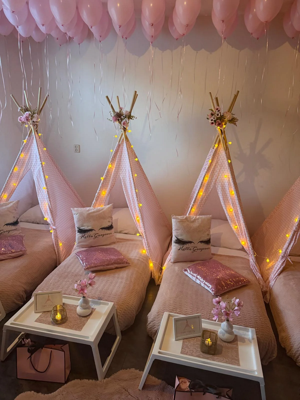 Girlpower tipi slaapfeestje: roze tipi’s met lampjes, wimperkussens en bedtafeltjes onder een plafond vol roze ballonnen