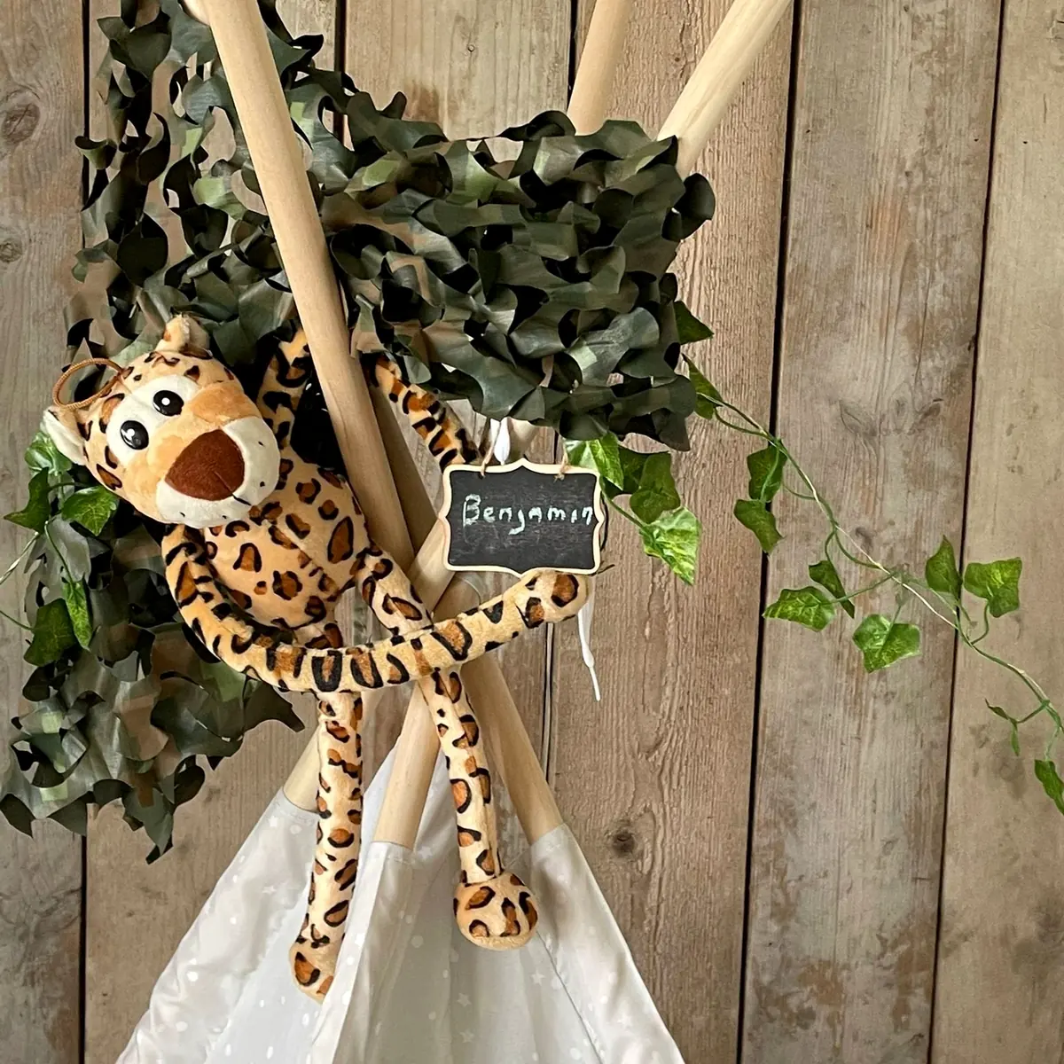 Knuffelluipaard met naambordje hangt aan de tipi tussen de bladeren