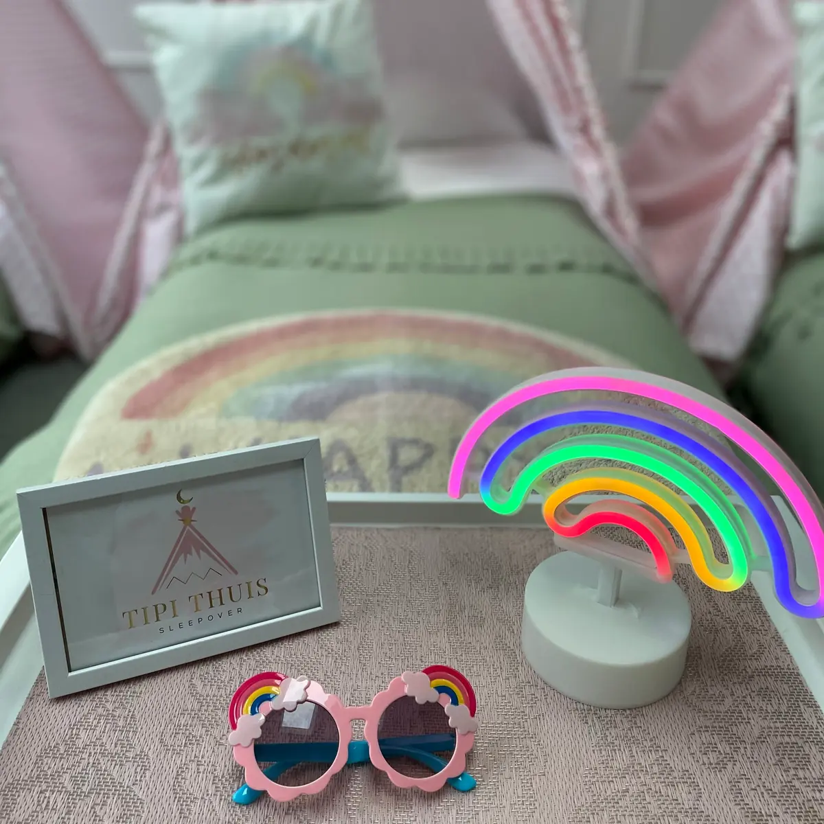 Rainbow thema: neon regenbooglamp, hartjeszonnebril en fotolijstje op het bed